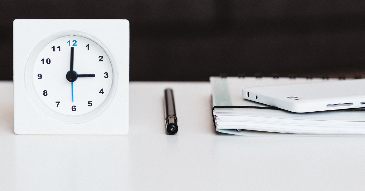 Small white clock, pen and binder on white desk