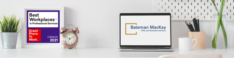 A white desk with a laptop that has the bateman mackay logo and the best workplaces logo