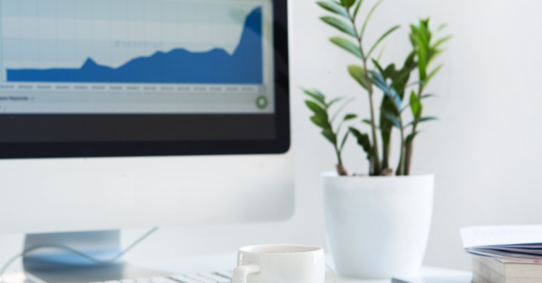 organized white desk with a mac and a fern