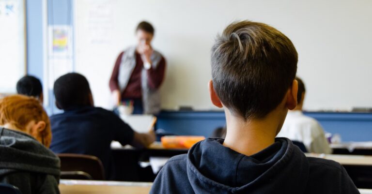 A classroom with a teacher at the front and students photographed from the back
