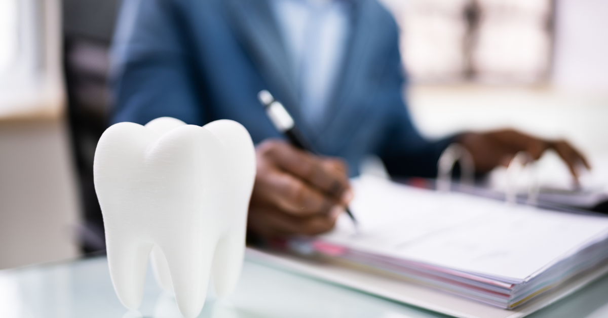 A closeup of someone signing papers with a large ornamental tooth in the foreground
