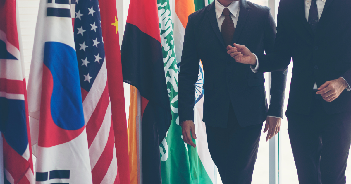 Two men in suits walking past several national flags