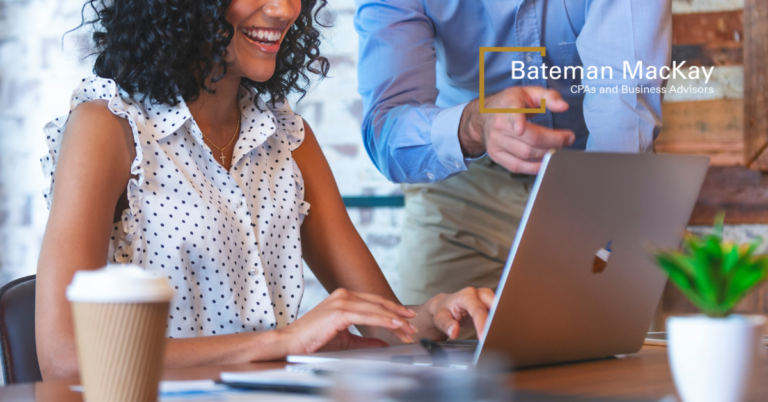 A woman sitting at a laptop with a man pointing at it. The Bateman MacKay logo is in the corner