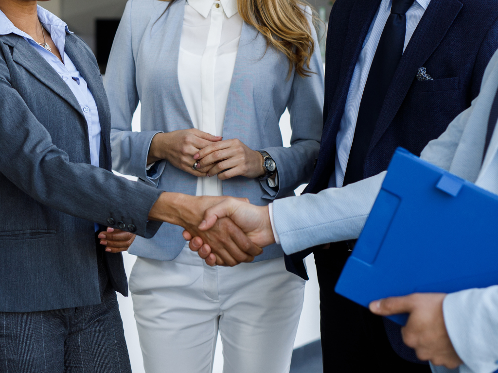 Four people, professionally, dressed with two shaking hands