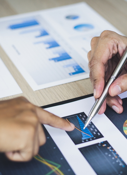 Graphs on a desk with one hand pointing and another using a pen