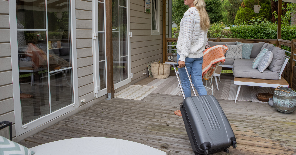 A blonde women rolling a suitcase across a deck towards a glass door