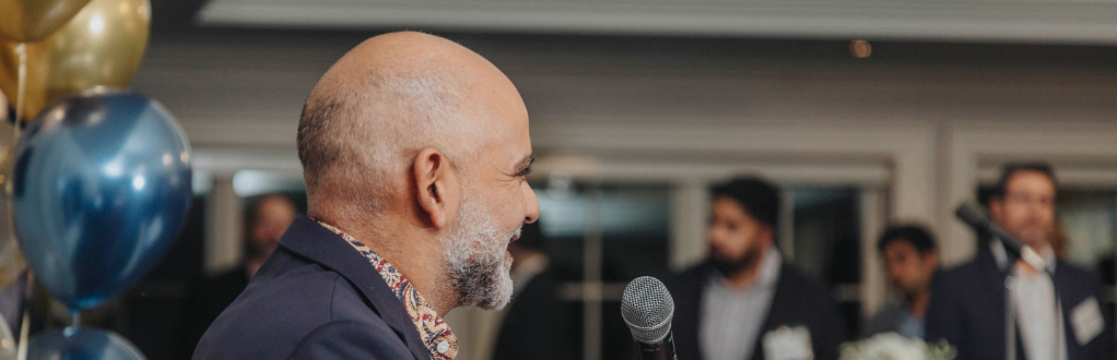 Vinay at a microphone speaking to an audience with balloons in the background